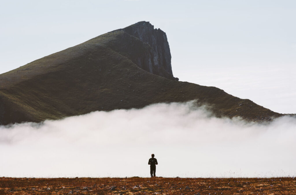 Landskapsbilde med fjell i bakgrunn. Person som ser utover tåken.
